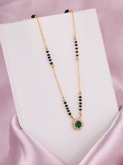 Necklace with green gemstone and black beads on a white stand against a pink background