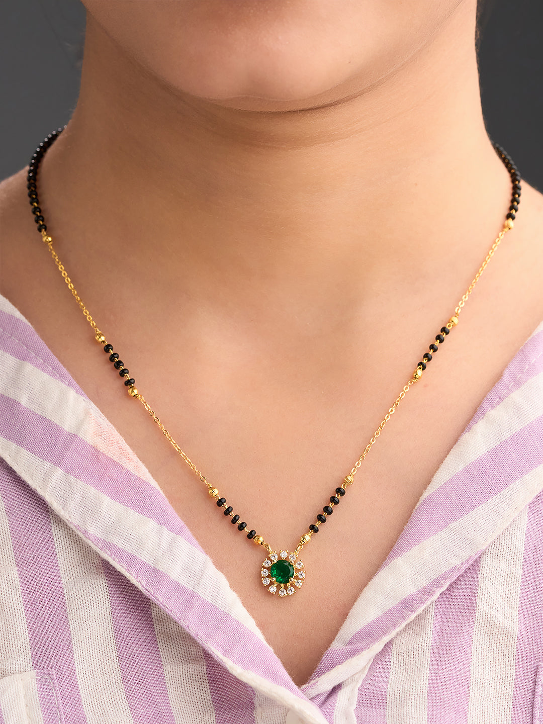 Necklace with a green pendant worn by a person in a striped shirt