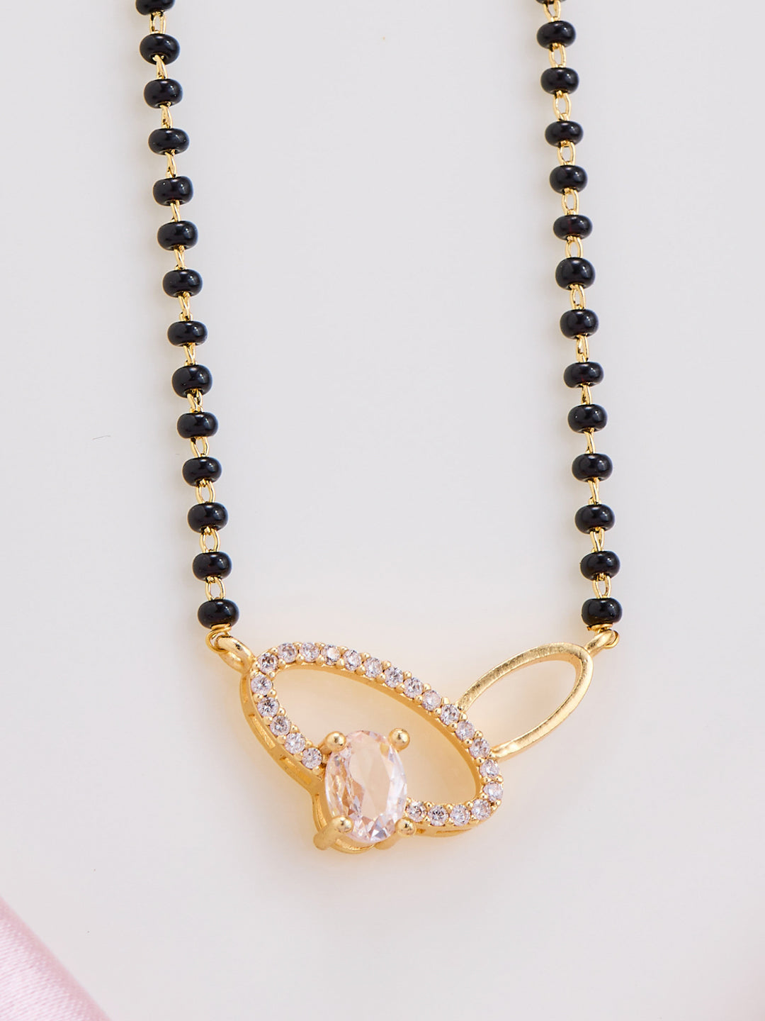 Necklace with black beads and a gold pendant on a light pink background