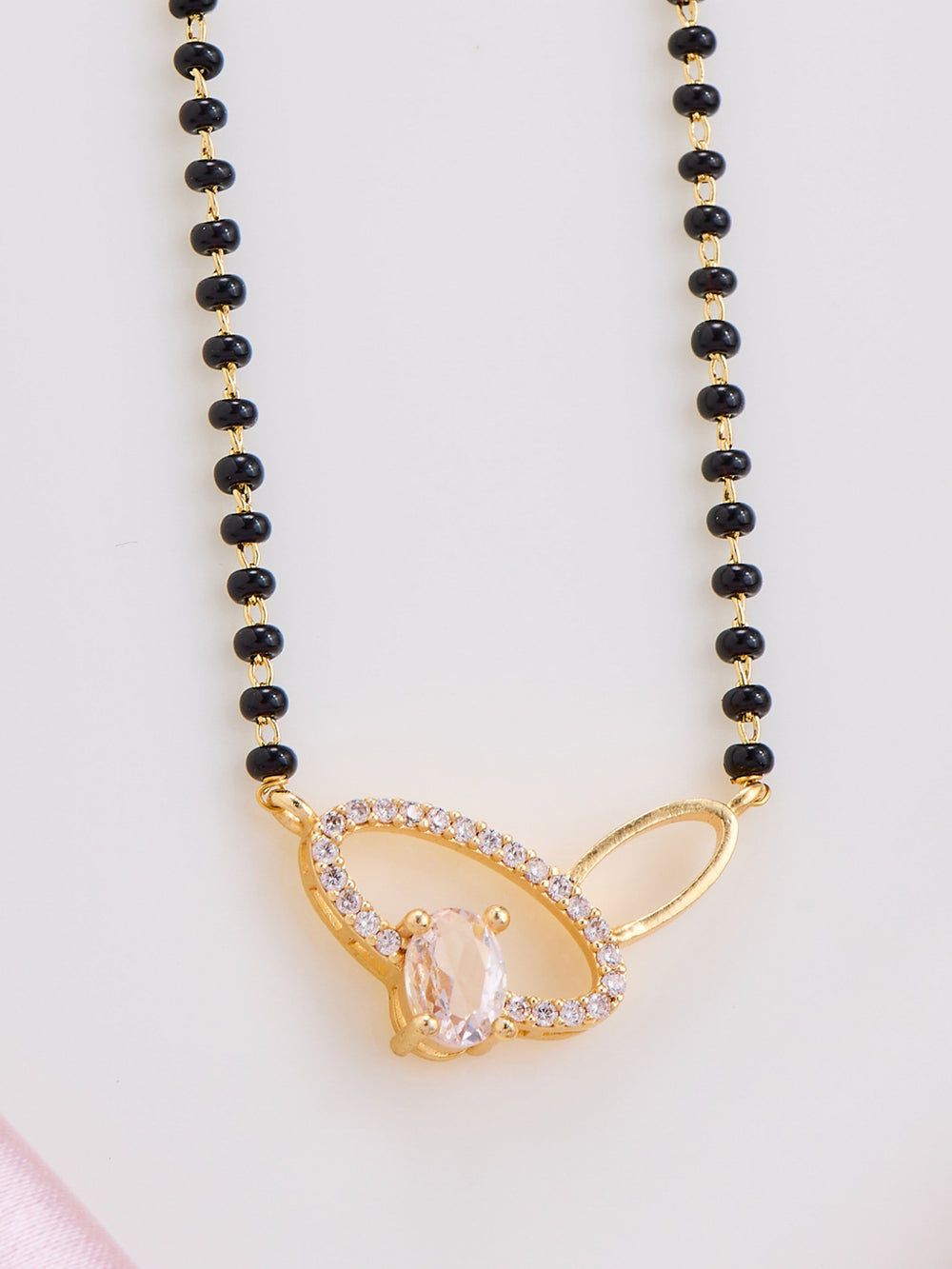 Necklace with black beads and a gold pendant on a light pink background
