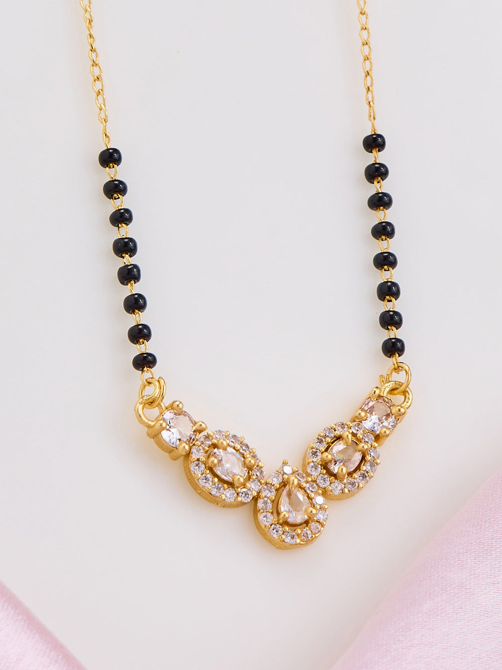 Gold necklace with black beads on a light pink background