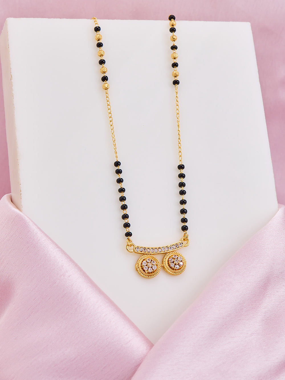 Necklace with black beads and gold pendants on a white stand with pink satin background