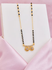 Necklace with black beads and gold pendants on a white stand with pink satin background