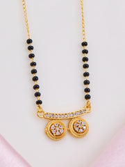 Gold necklace with black beads and decorative elements on a light pink background