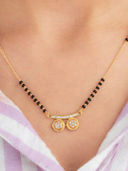 Gold necklace with black beads and circular pendant on a person wearing a light purple top.