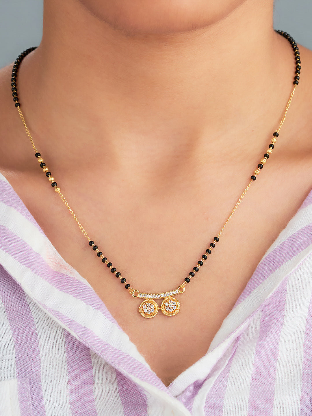 Gold necklace with black beads and a pendant on a person wearing a striped shirt.