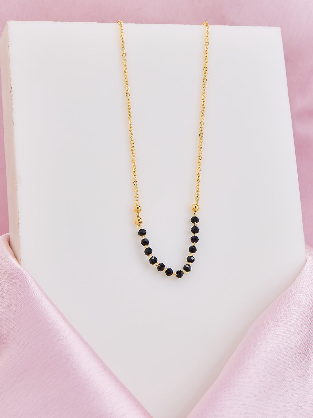 Gold necklace with black beads on a white card with pink border