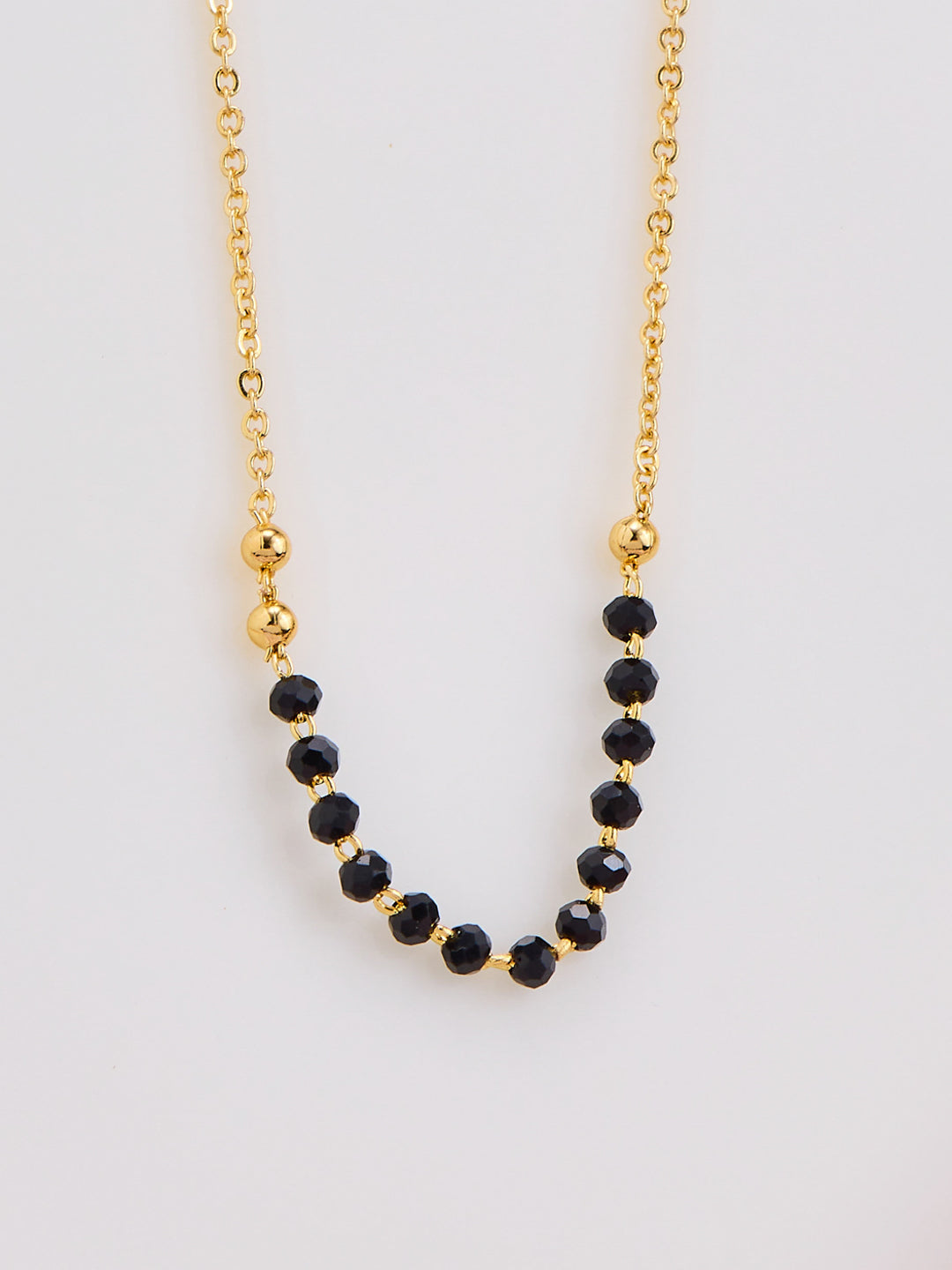 Gold necklace with black beads on a light gray background