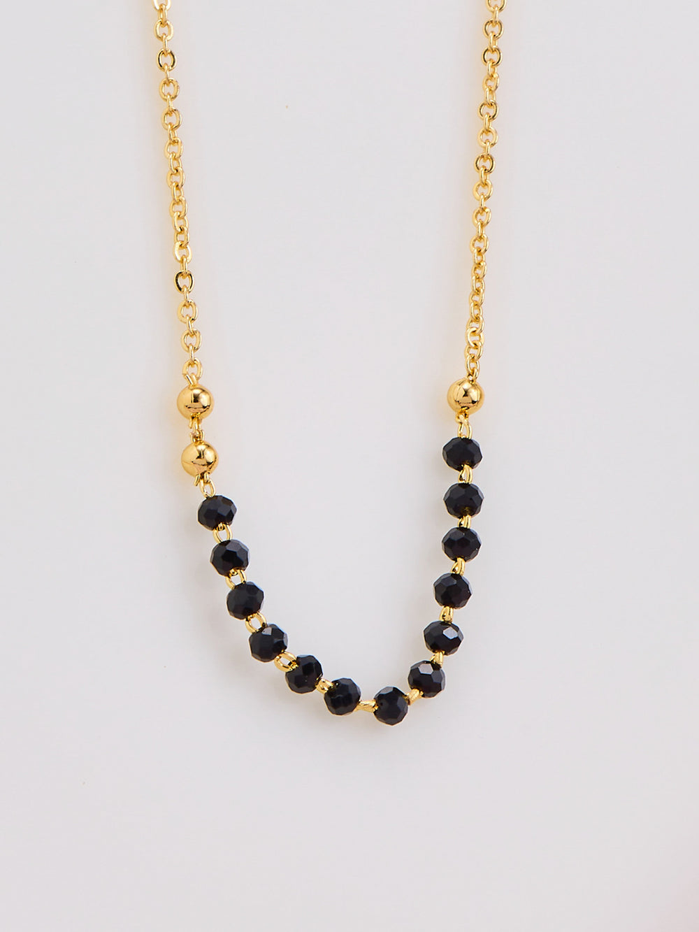 Gold necklace with black beads on a light gray background