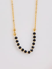 Gold necklace with black beads on a light gray background
