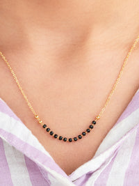 Gold necklace with black beads worn by a person against a light background