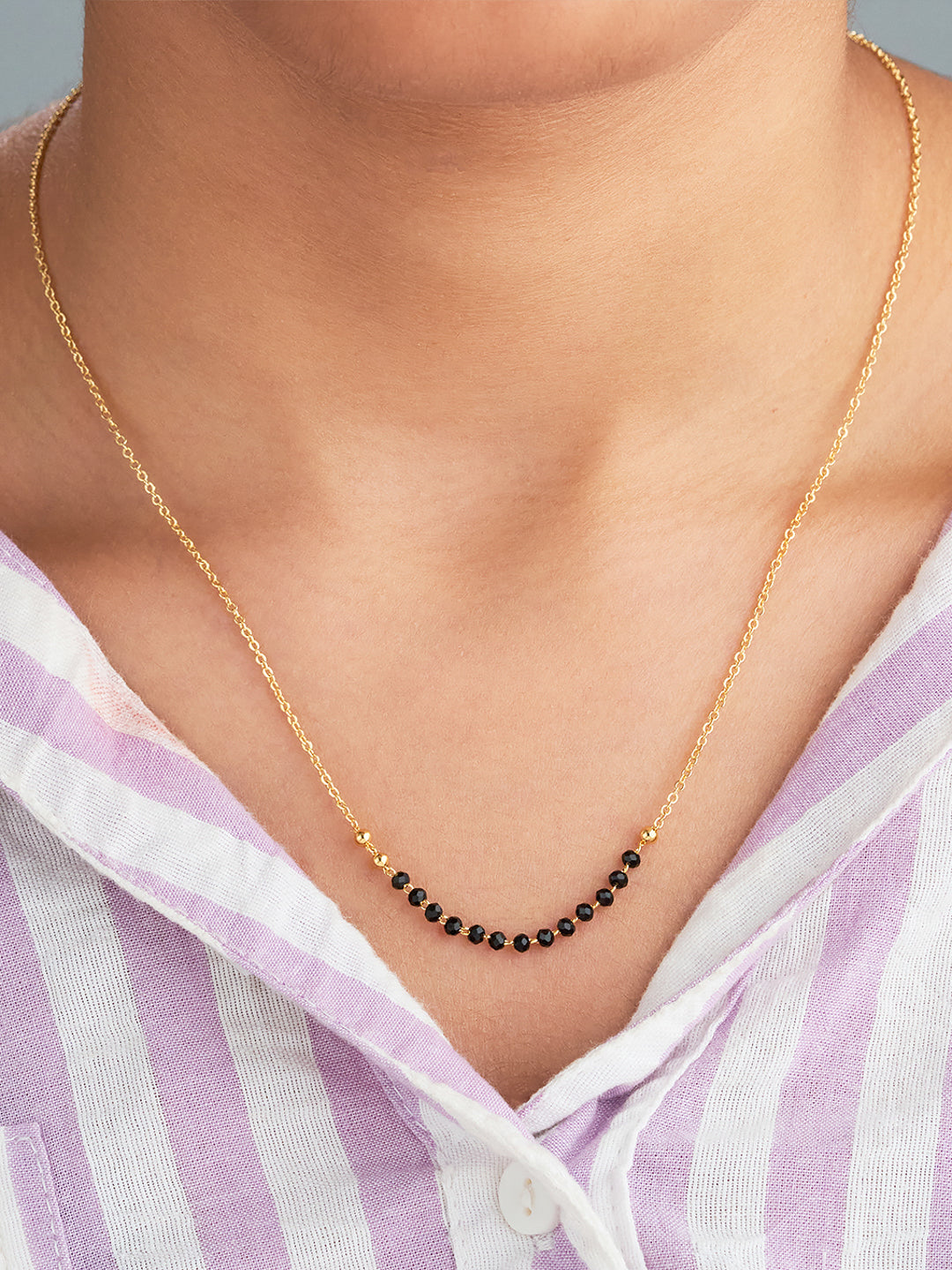 Gold necklace with black beads worn by a person in a striped shirt.