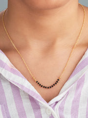 Gold necklace with black beads worn by a person in a striped shirt.