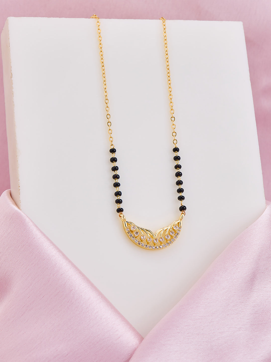 Gold necklace with black beads on a white stand against a pink background