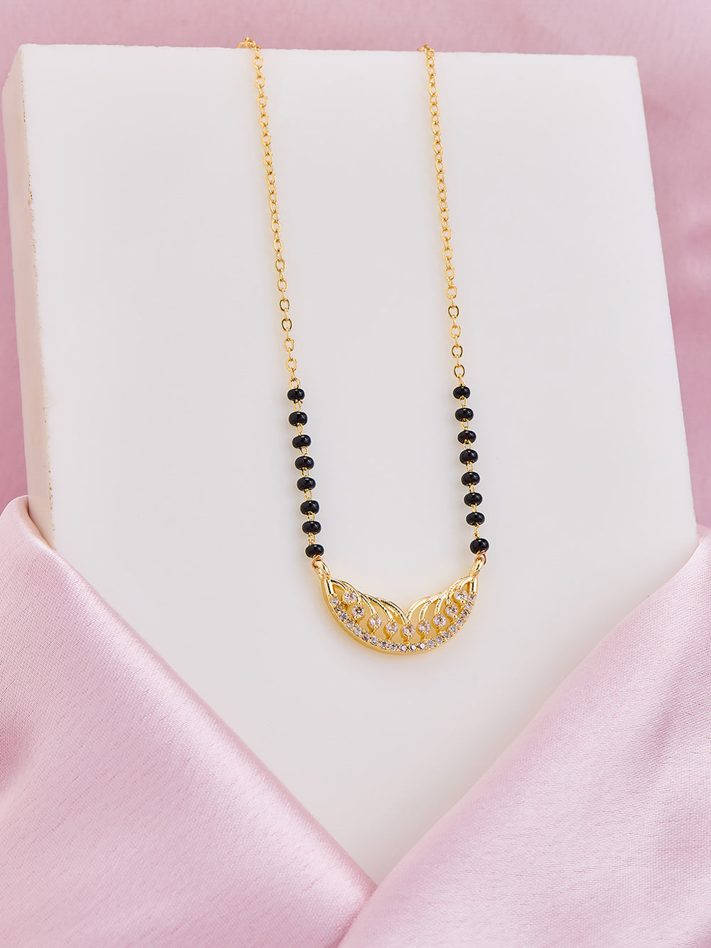 Gold necklace with black beads on a white stand against a pink background