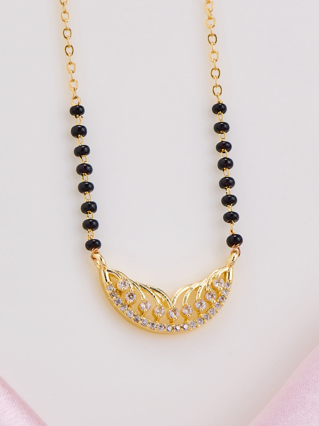 Gold necklace with black beads on a light pink background