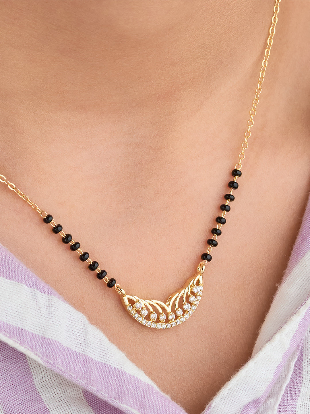 Gold necklace with black beads on a person wearing a light purple garment.