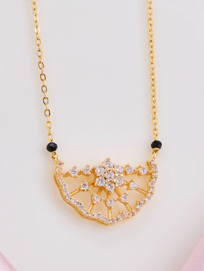 Gold necklace with a decorative pendant on a light pink background