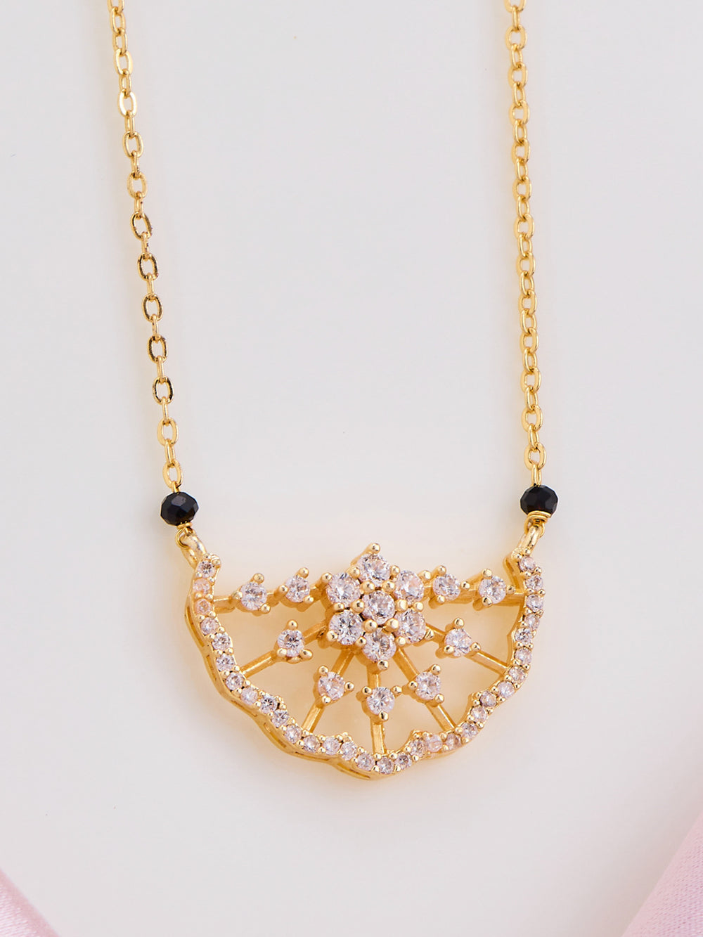 Gold necklace with a decorative pendant on a light pink background