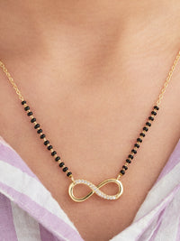 Gold necklace with an infinity symbol pendant on a person wearing a light purple garment.