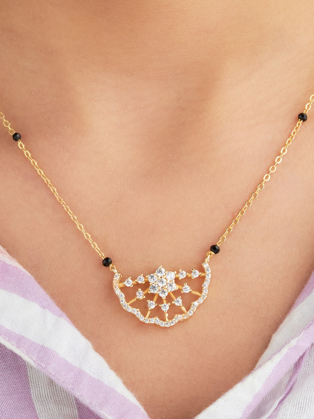 Gold necklace with a decorative pendant on a person wearing a light purple top.