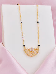 Gold necklace with a floral pendant on a white stand against a pink background