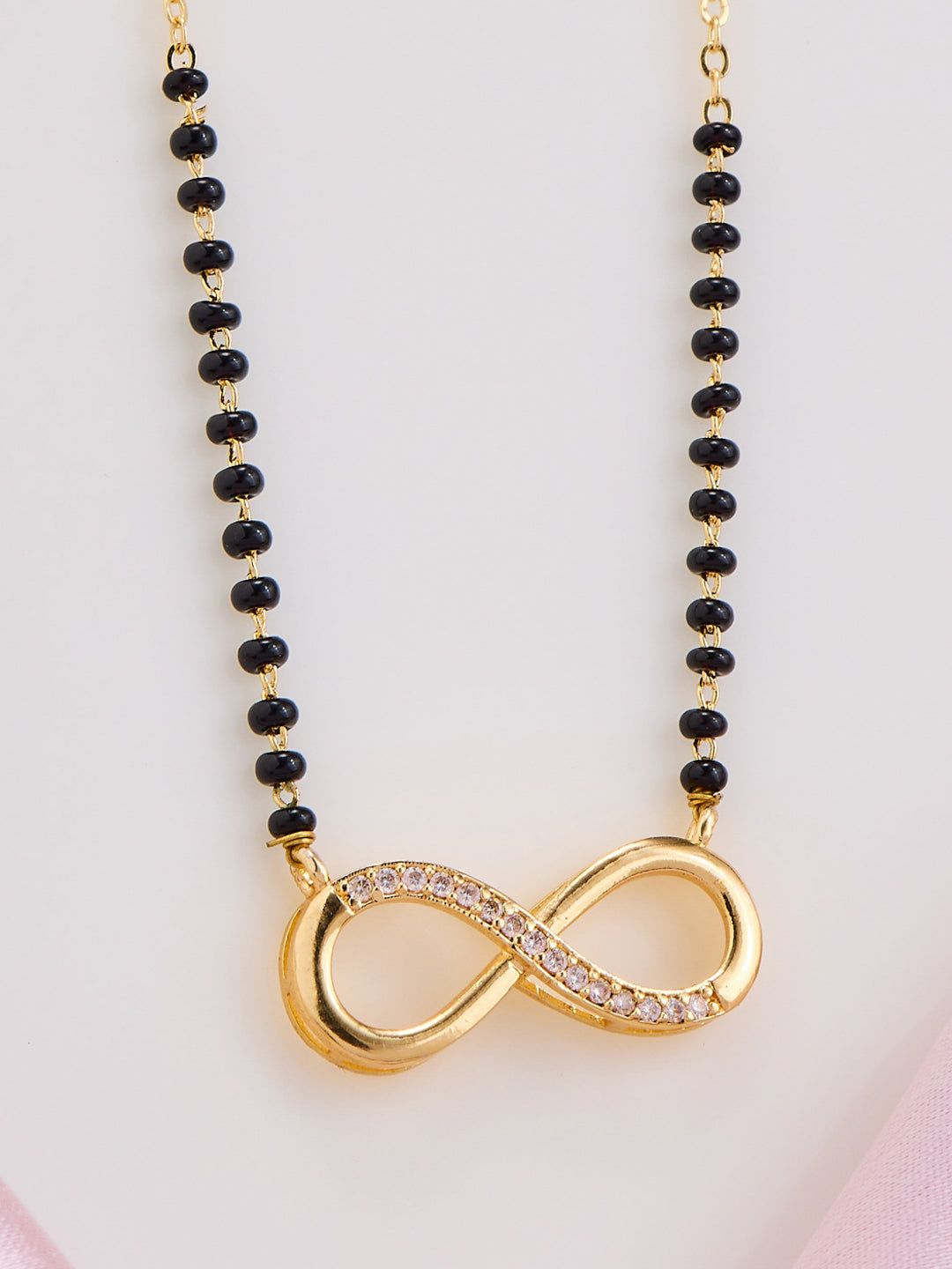 Necklace with black beads and a gold infinity symbol pendant on a light pink background