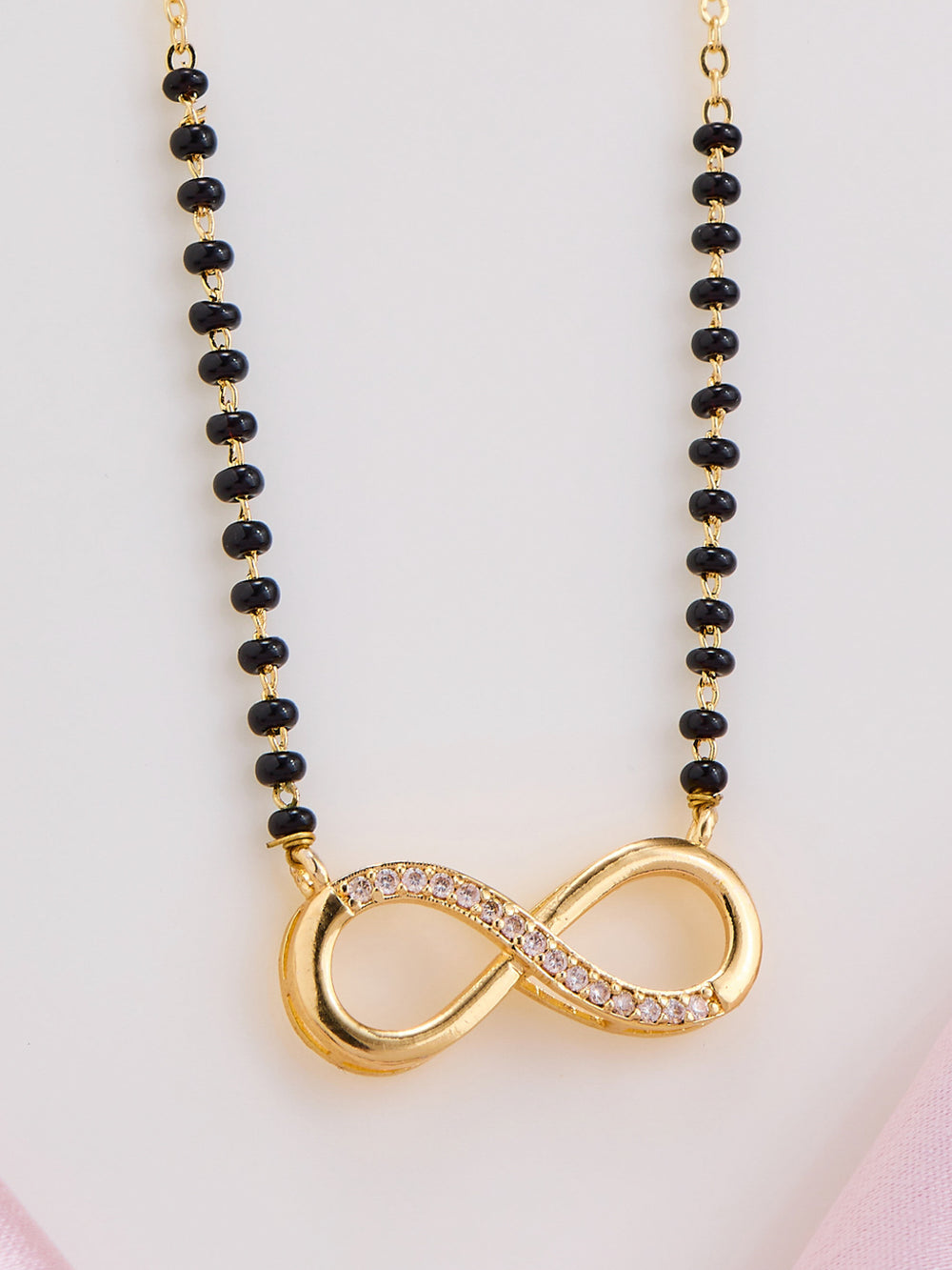 Necklace with black beads and a gold infinity symbol pendant on a light pink background