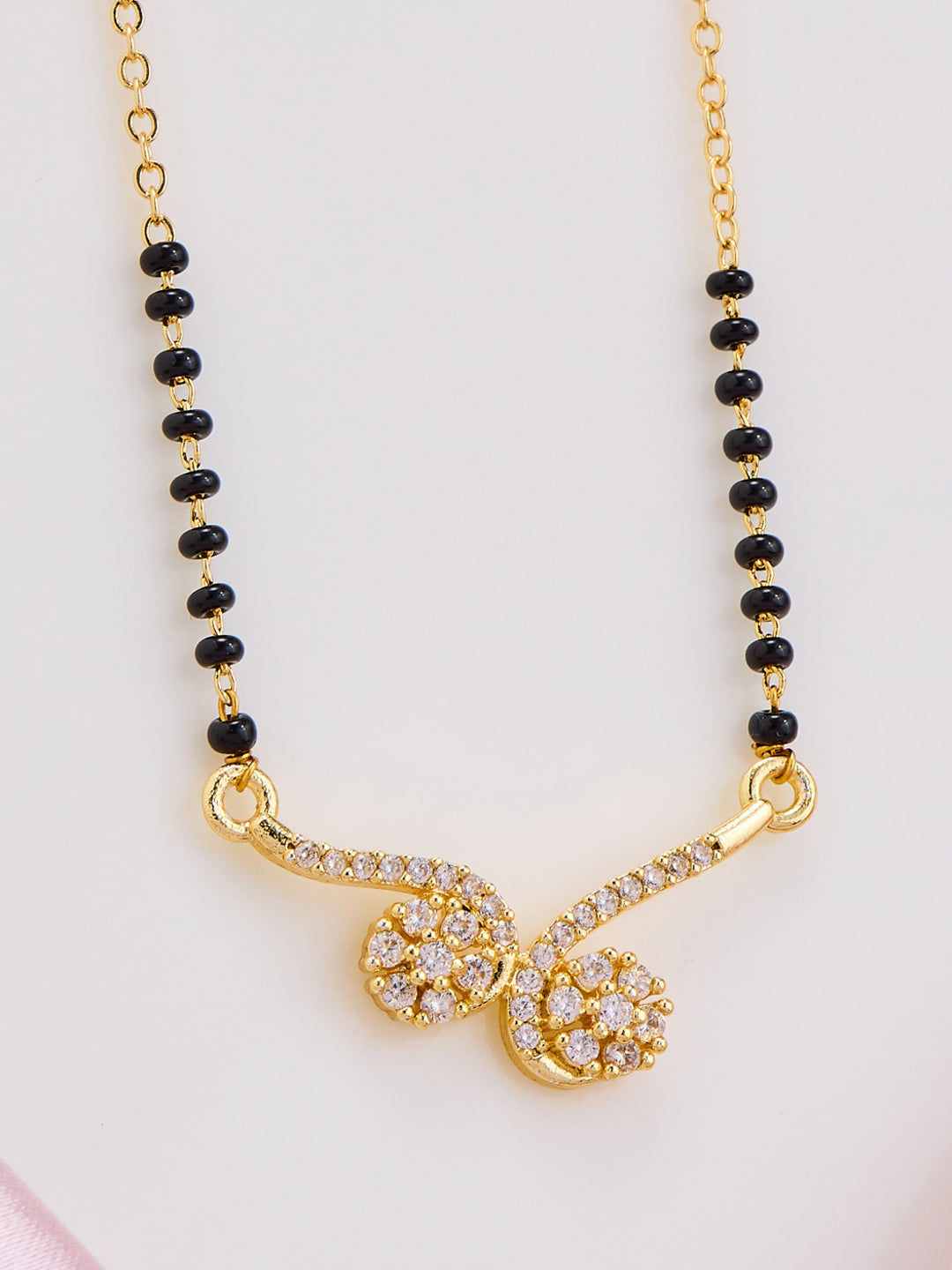 Gold necklace with black beads and a decorative clasp on a light pink background