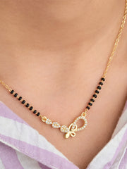 Gold necklace with black beads and a decorative clasp on a person wearing a light purple garment.