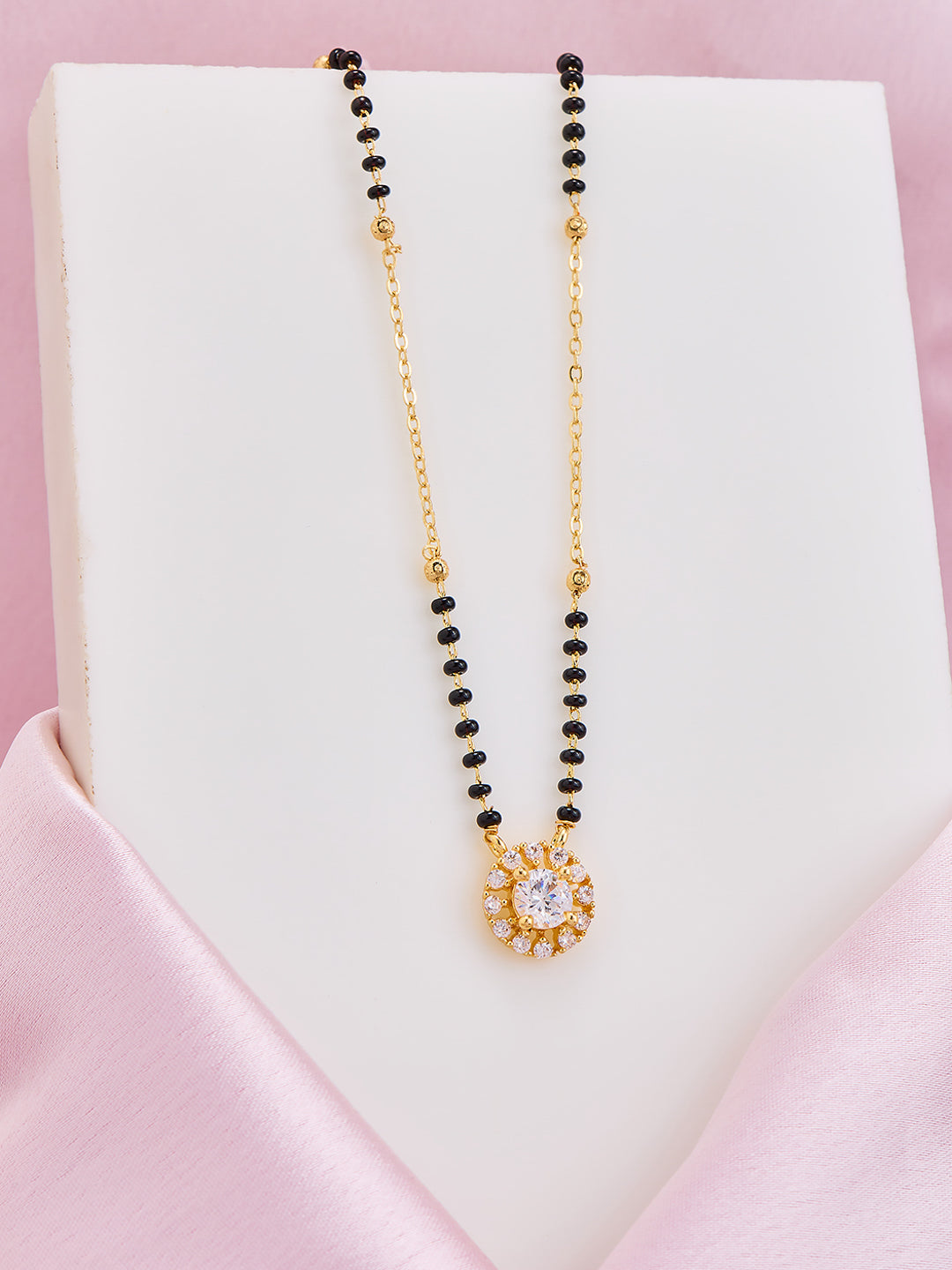 Black beaded necklace with a gold chain and pendant on a white stand with pink background
