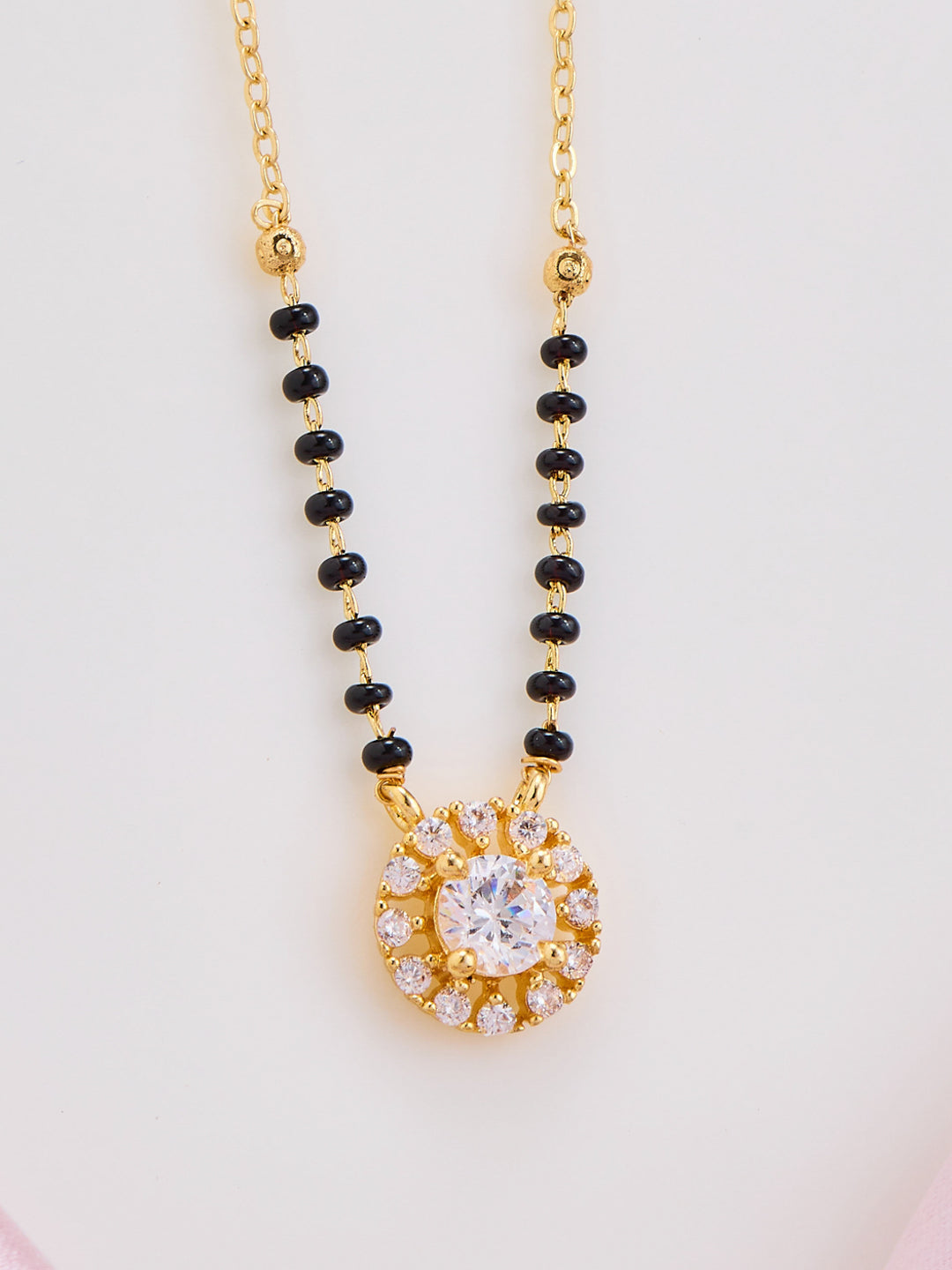 Necklace with black beads and a gold pendant on a light gray background