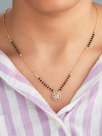 Gold necklace with a central pendant worn by a person in a striped shirt.