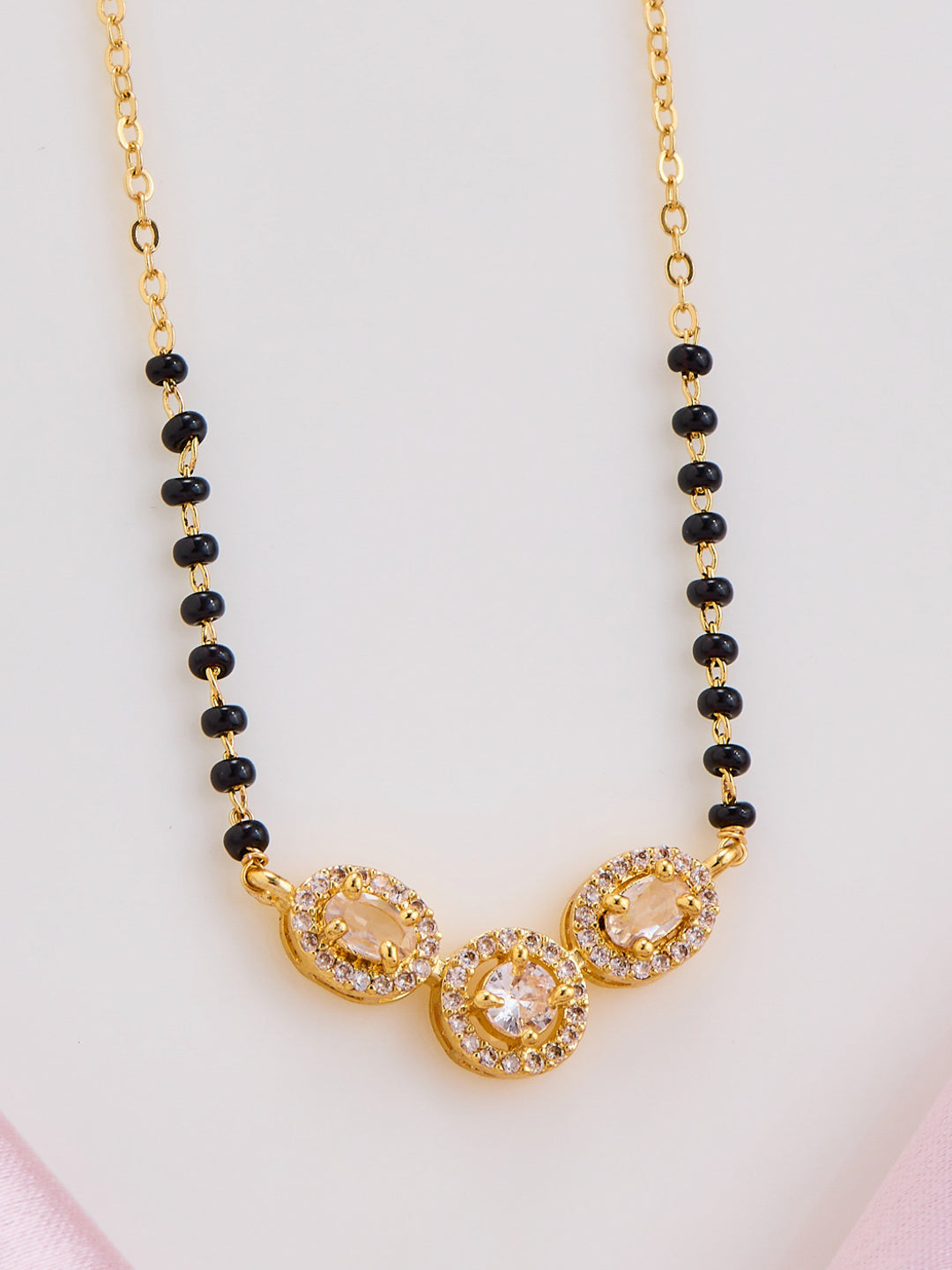 Gold necklace with black beads on a light pink background