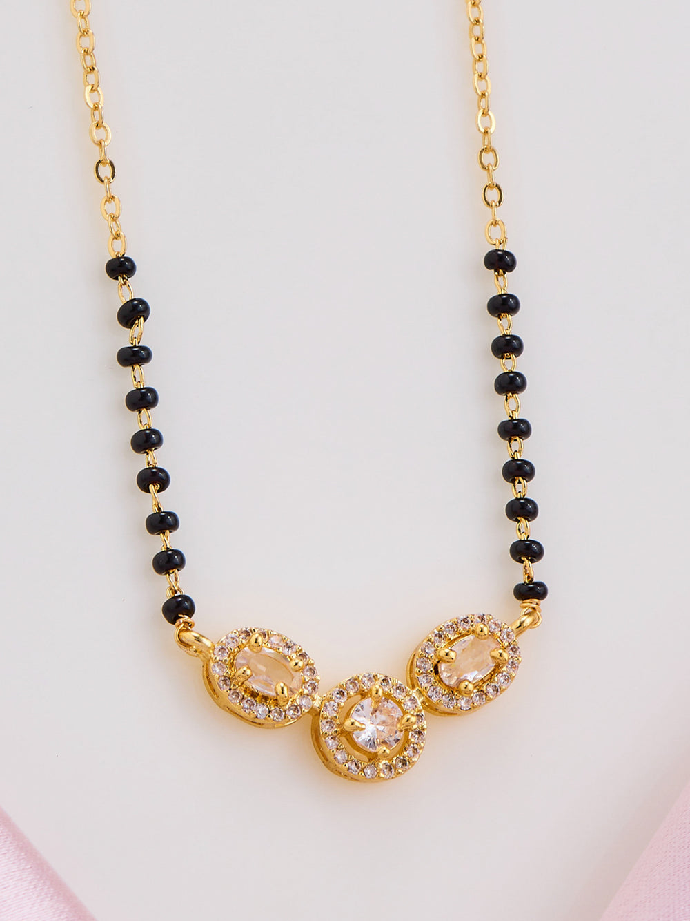 Gold necklace with black beads on a light pink background