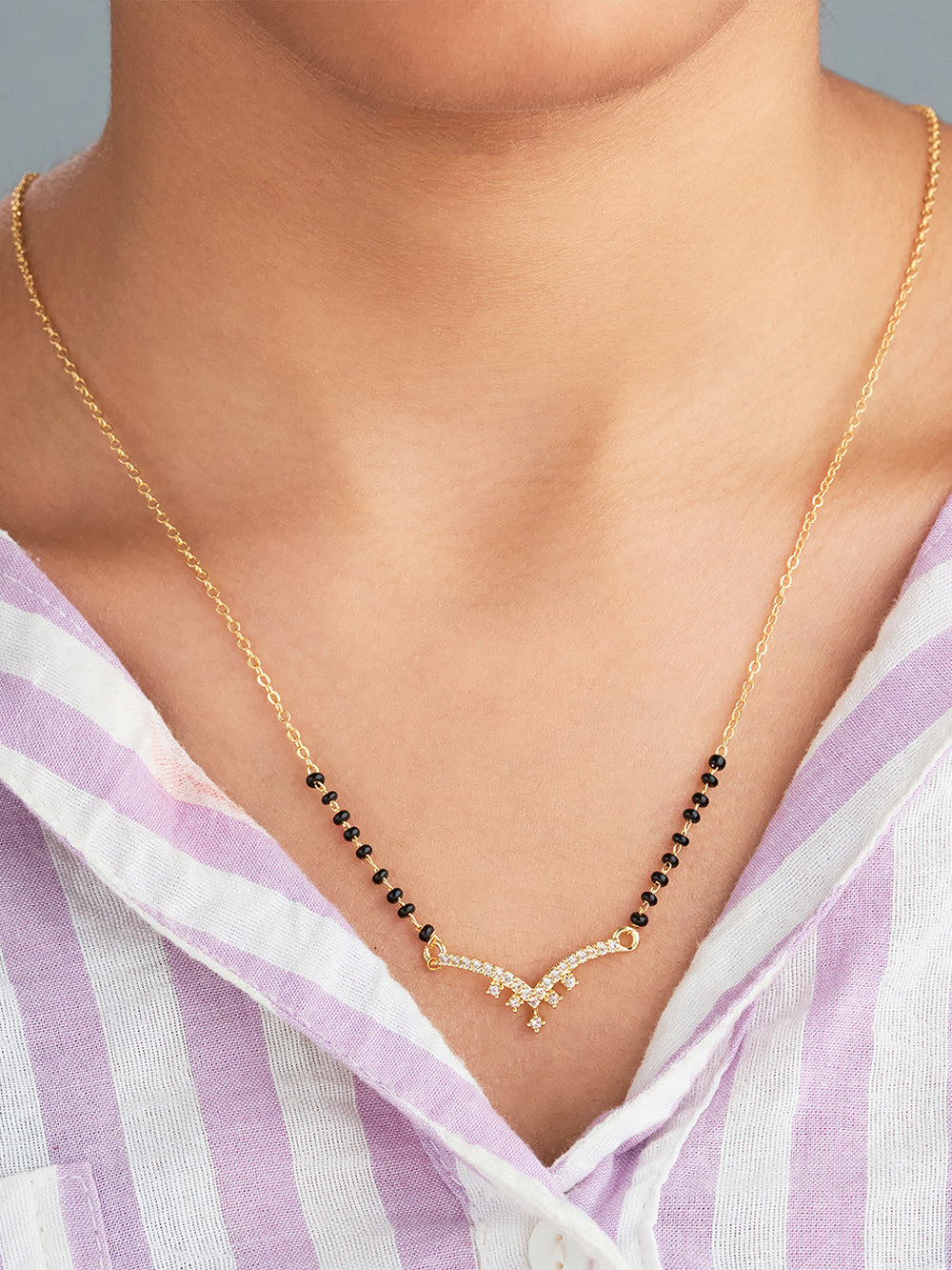 Gold necklace with black beads worn by a person in a striped shirt.