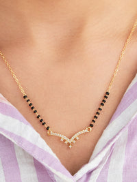 Gold necklace with black beads on a person wearing a light purple and white striped garment.
