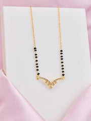 Necklace with black beads and gold clasp on a white box with pink background