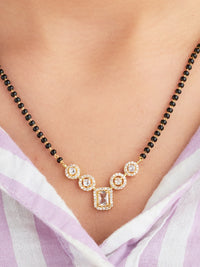 Gold necklace with black beads on a person wearing a light purple garment.