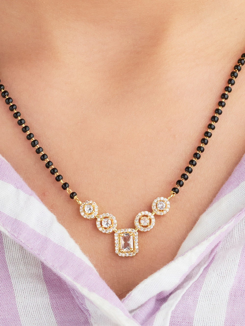 Gold necklace with black beads on a person wearing a light purple garment.