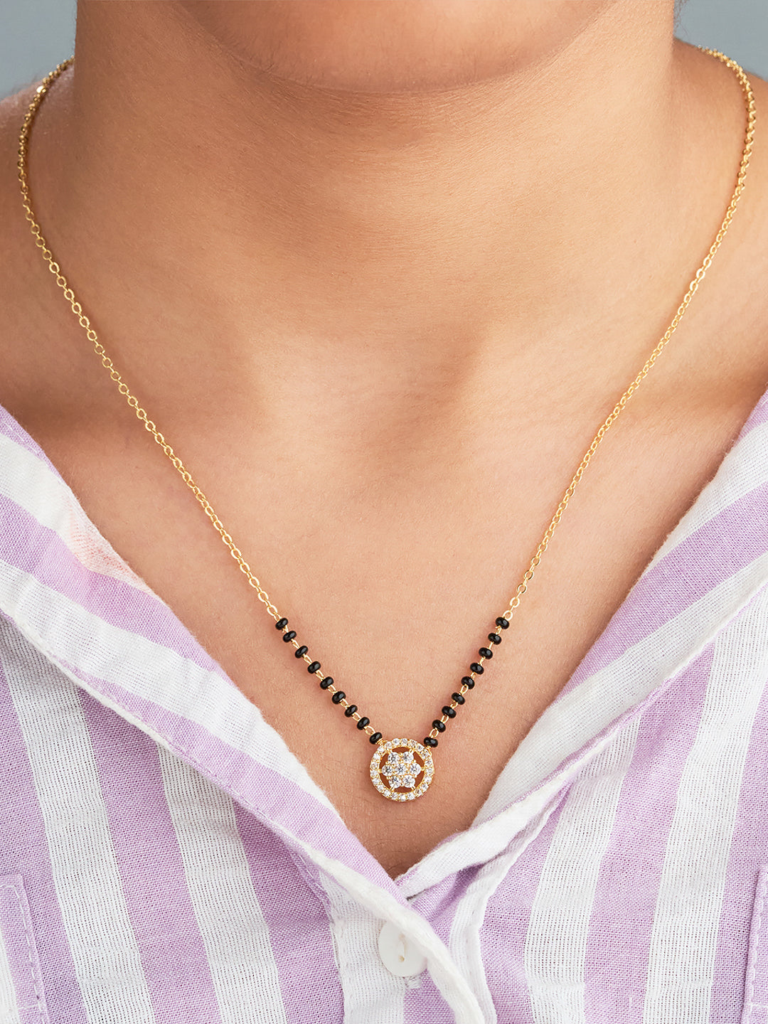 Gold necklace with a central pendant worn by a person in a striped shirt.