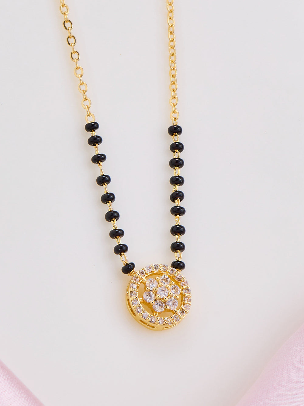 Necklace with black beads and a gold pendant on a light pink background