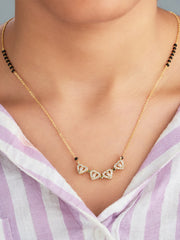 Gold necklace with heart-shaped gemstones worn by a person in a striped shirt.
