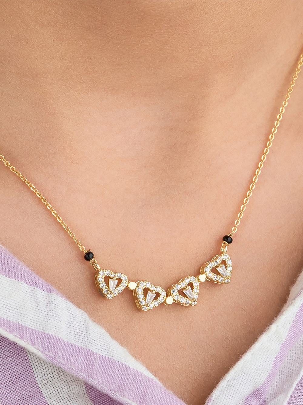 Gold necklace with heart-shaped pendants on a person wearing a light purple garment.