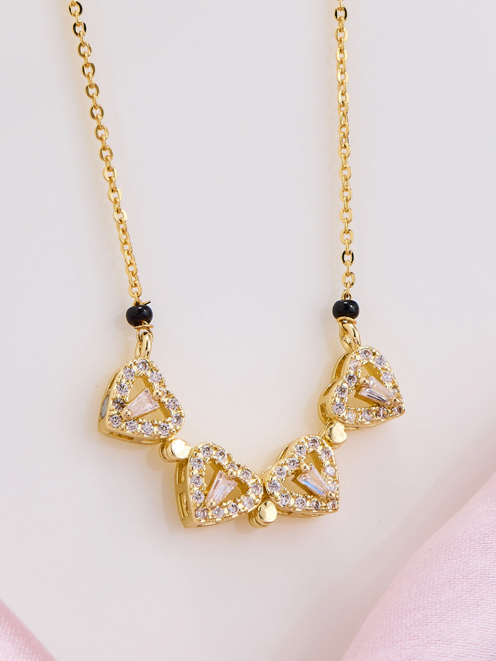 Gold necklace with triangular pendants on a light pink background