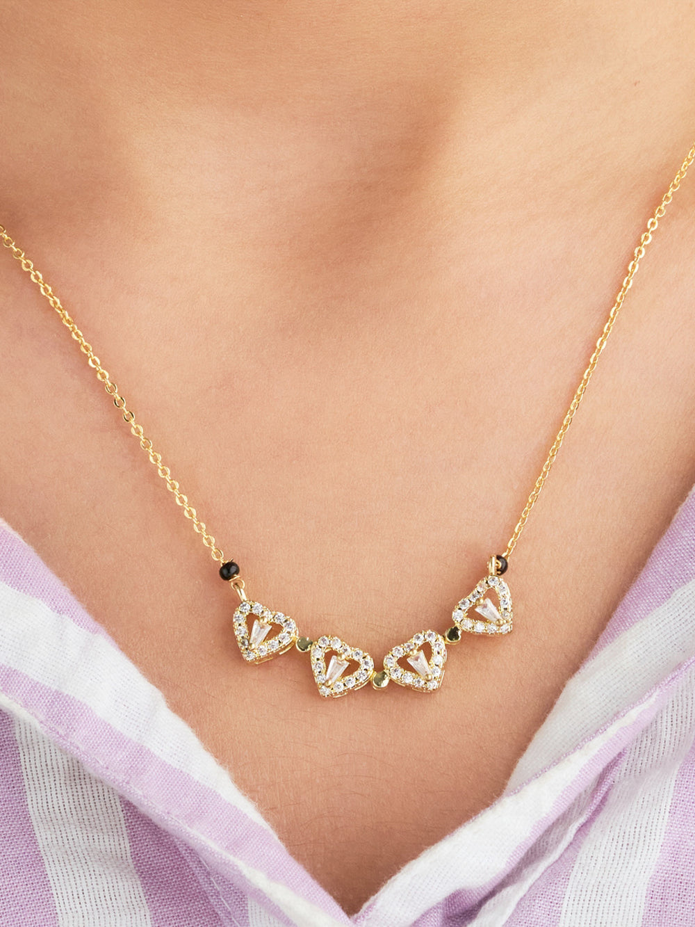 Gold necklace with heart-shaped pendants on a person wearing a light purple top.