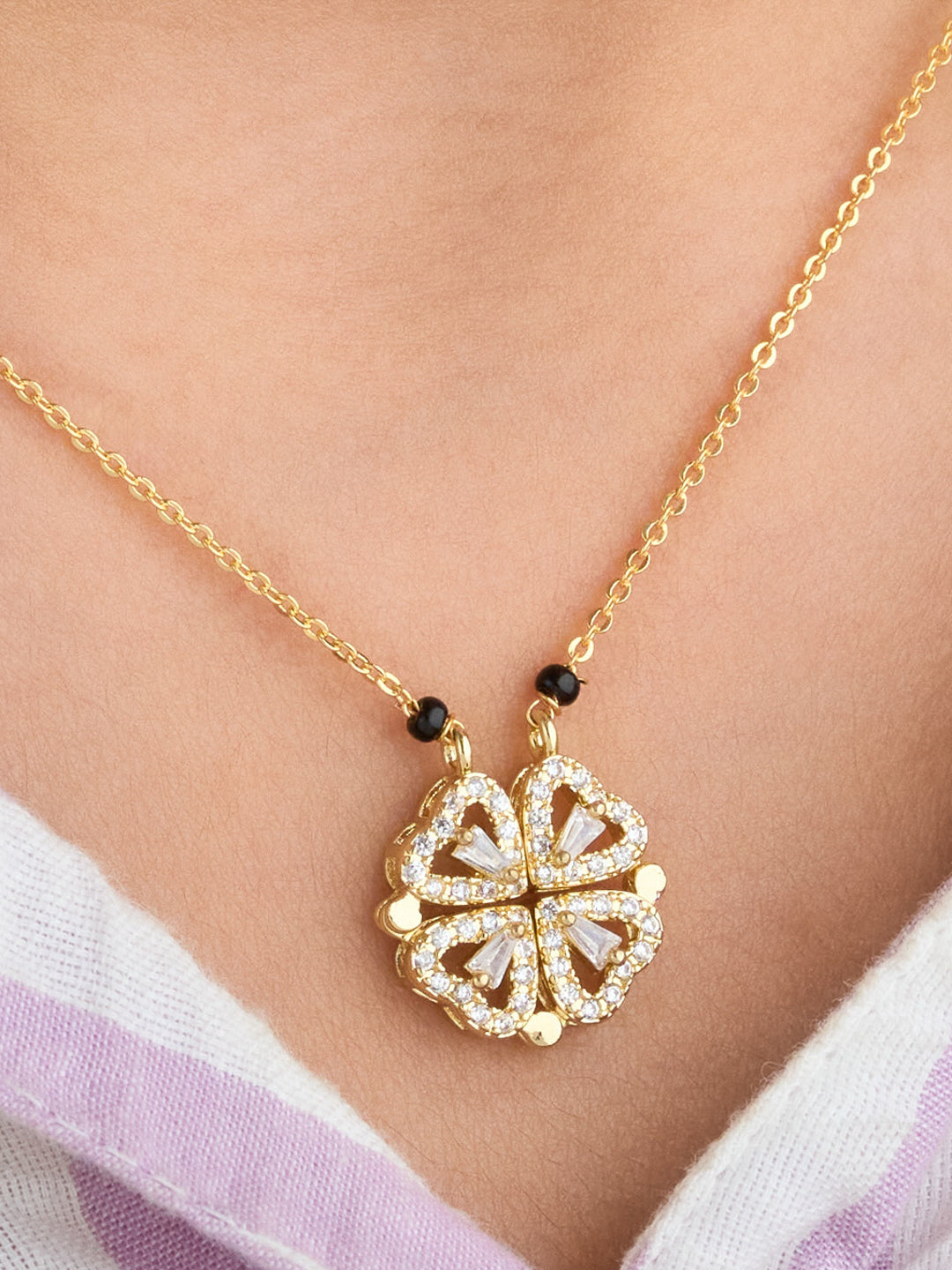 Gold necklace with a floral pendant on a person wearing a white and purple garment.