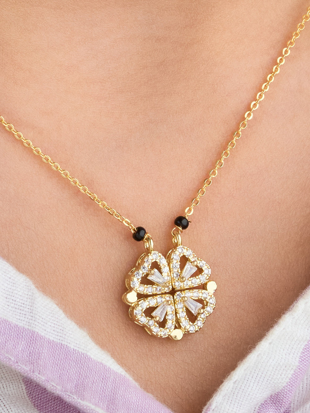 Gold necklace with a floral pendant on a person wearing a white and purple garment.