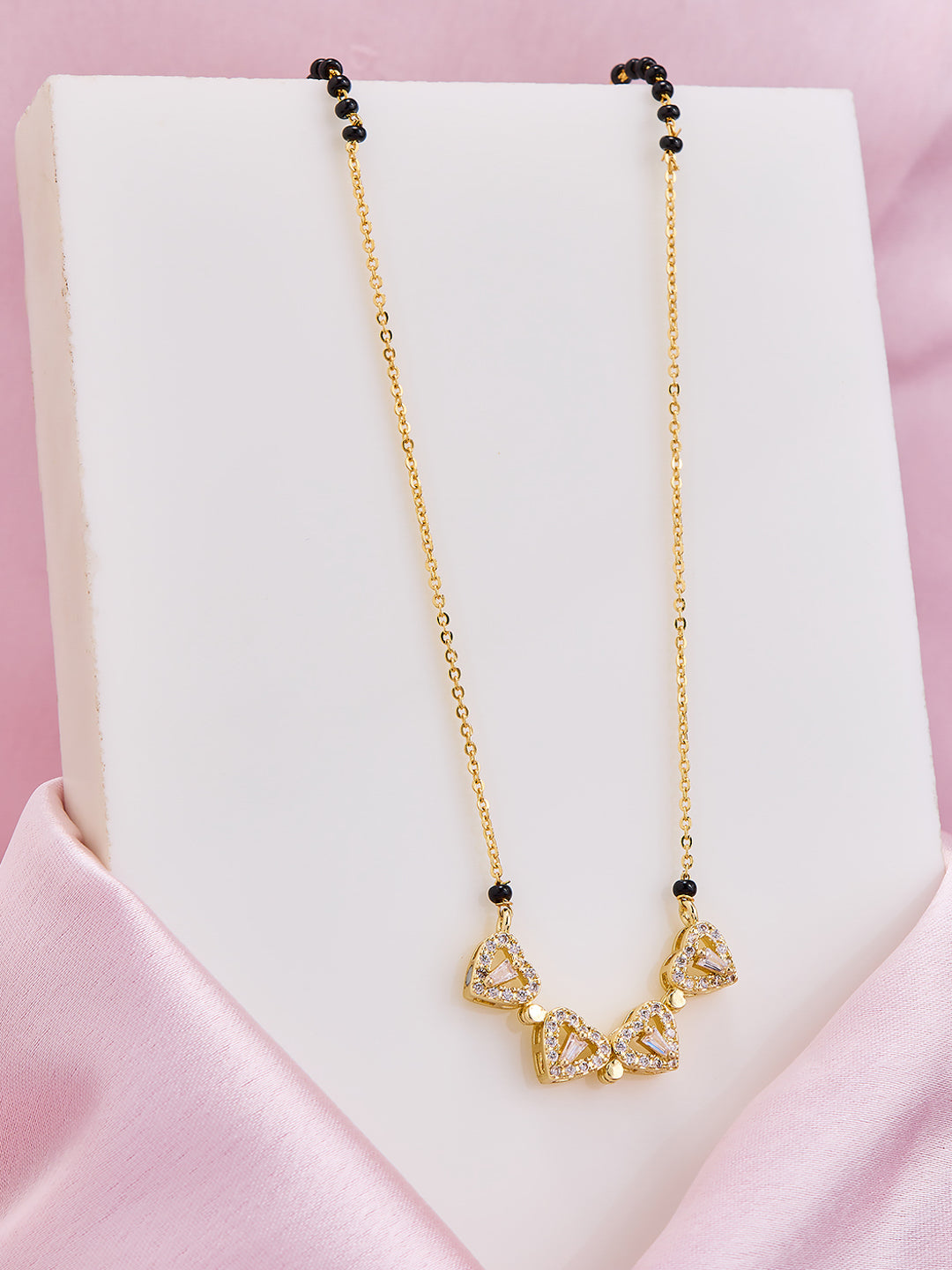 Gold necklace with black beads on a white stand against a pink satin background