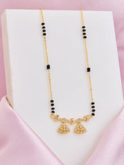 Gold necklace with black beads on a white stand against a pink background